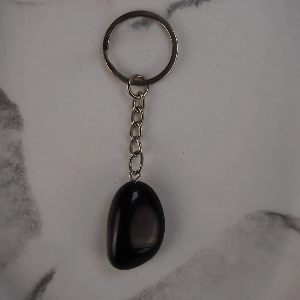 Obsidian Trommelstein Schlüsselanhänger auf Marmorhintergrund