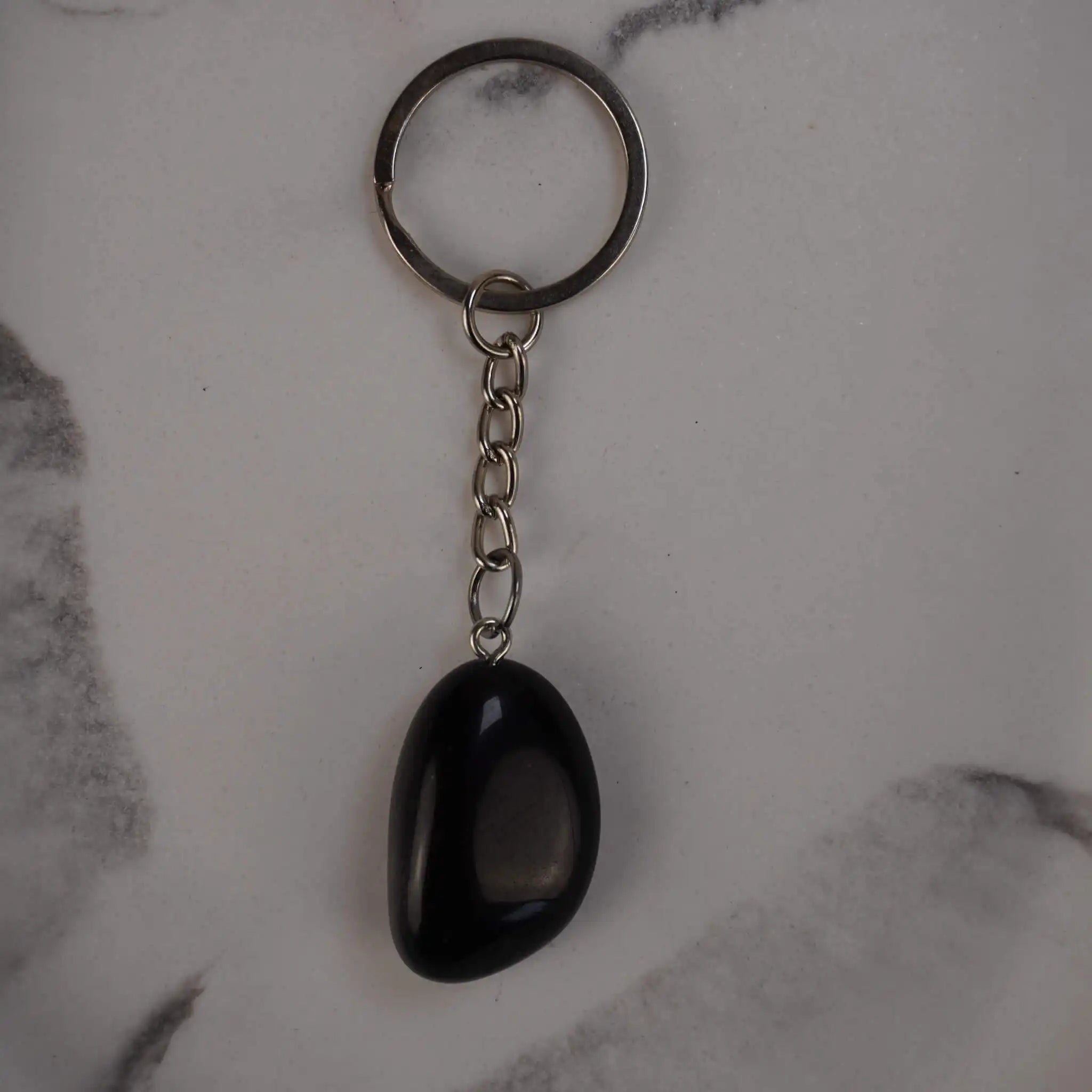 Obsidian Trommelstein Schlüsselanhänger auf Marmorhintergrund