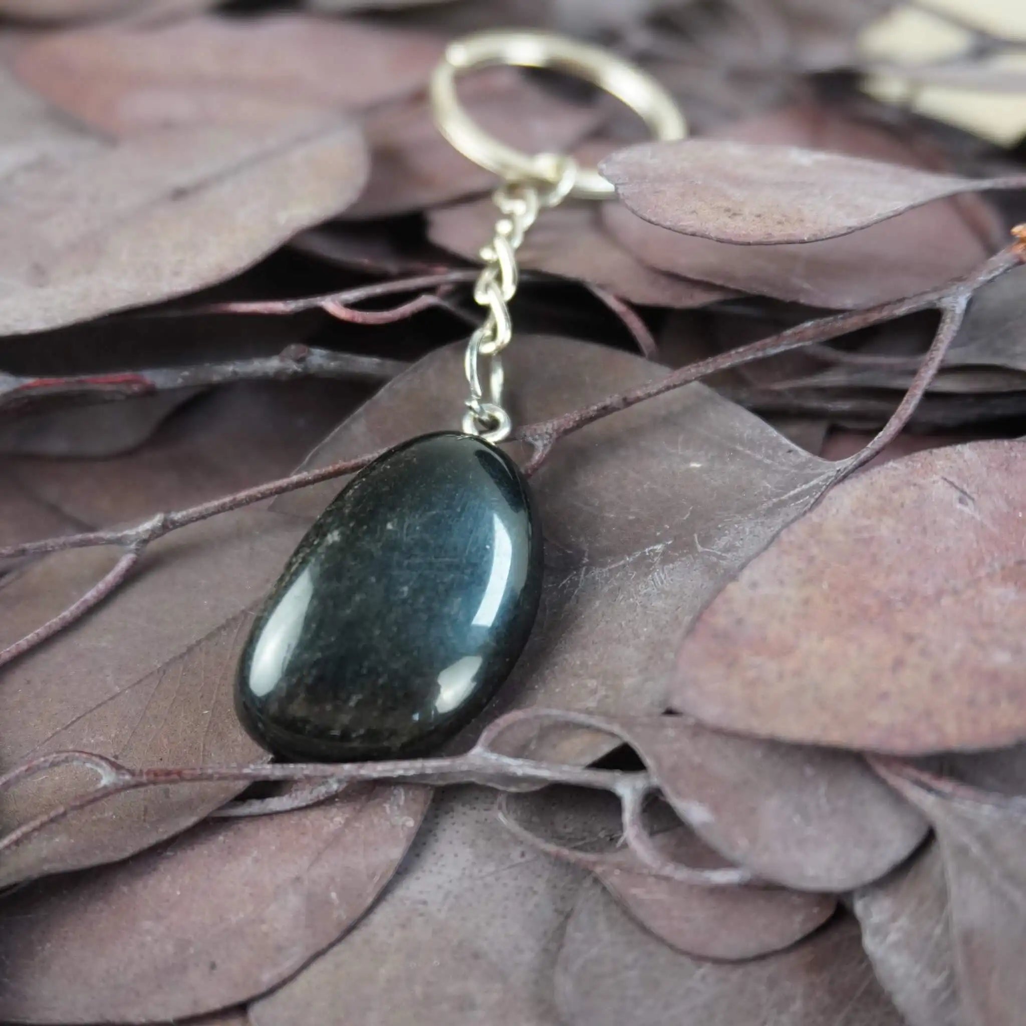Obsidian Trommelstein Schlüsselanhänger auf dunklen Blättern
