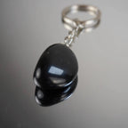 Obsidian Trommelstein Schlüsselanhänger mit Spiegelung auf Glasfläche