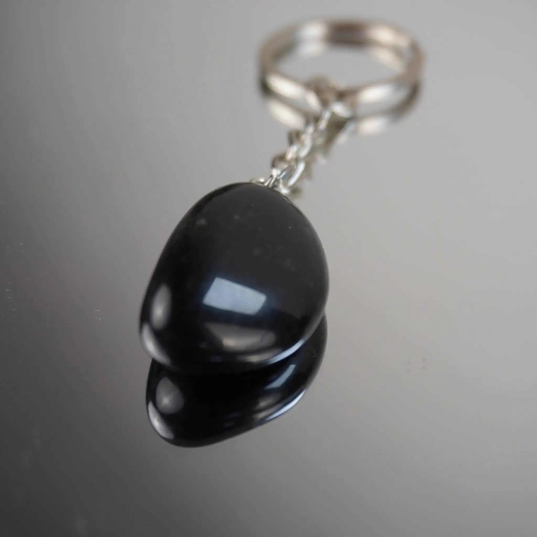 Obsidian Trommelstein Schlüsselanhänger mit Spiegelung auf Glasfläche