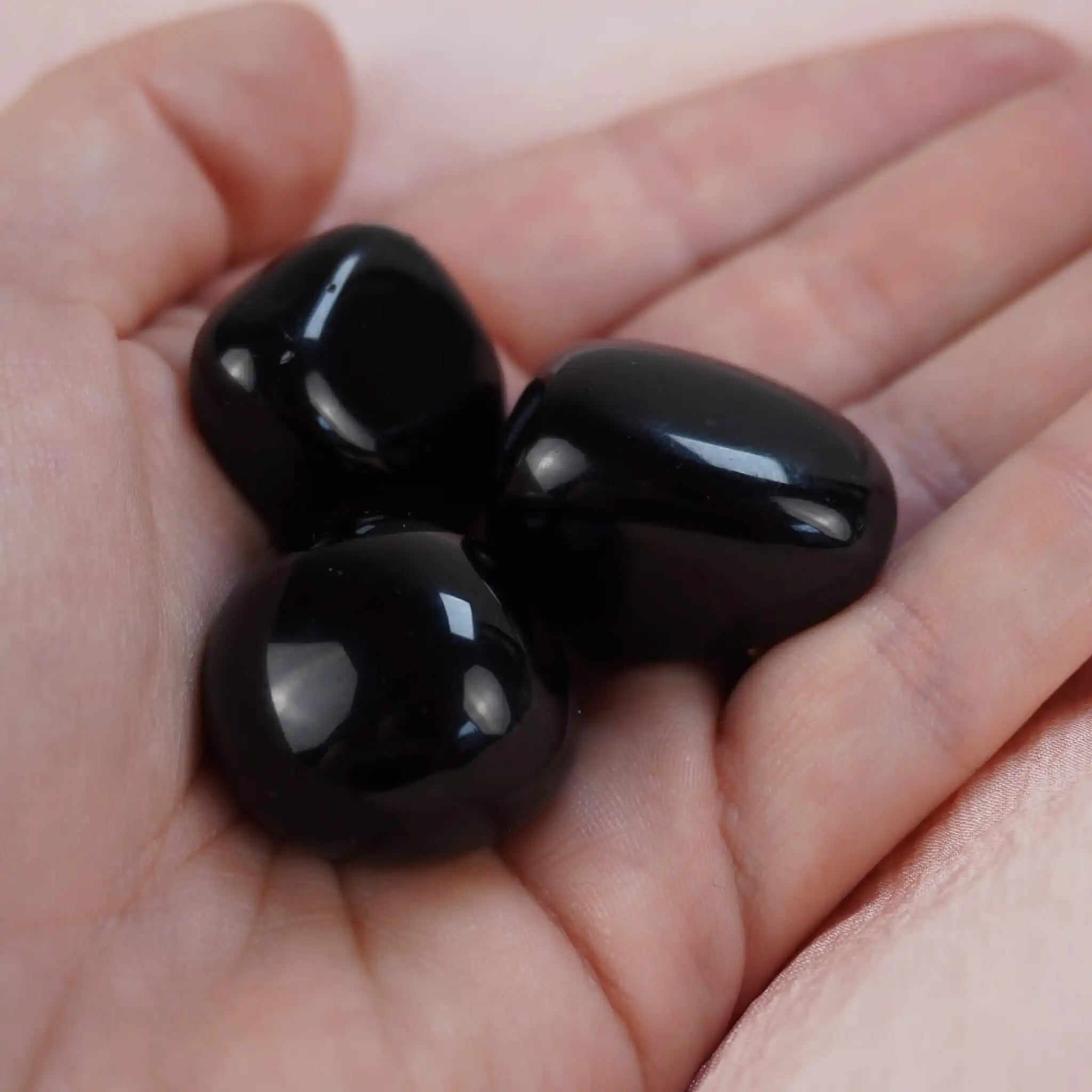 Drei schwarze Obsidian Trommelsteine in der Hand gehalten