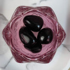 Vier schwarze Obsidian Trommelsteine in einer rosa Glasschale