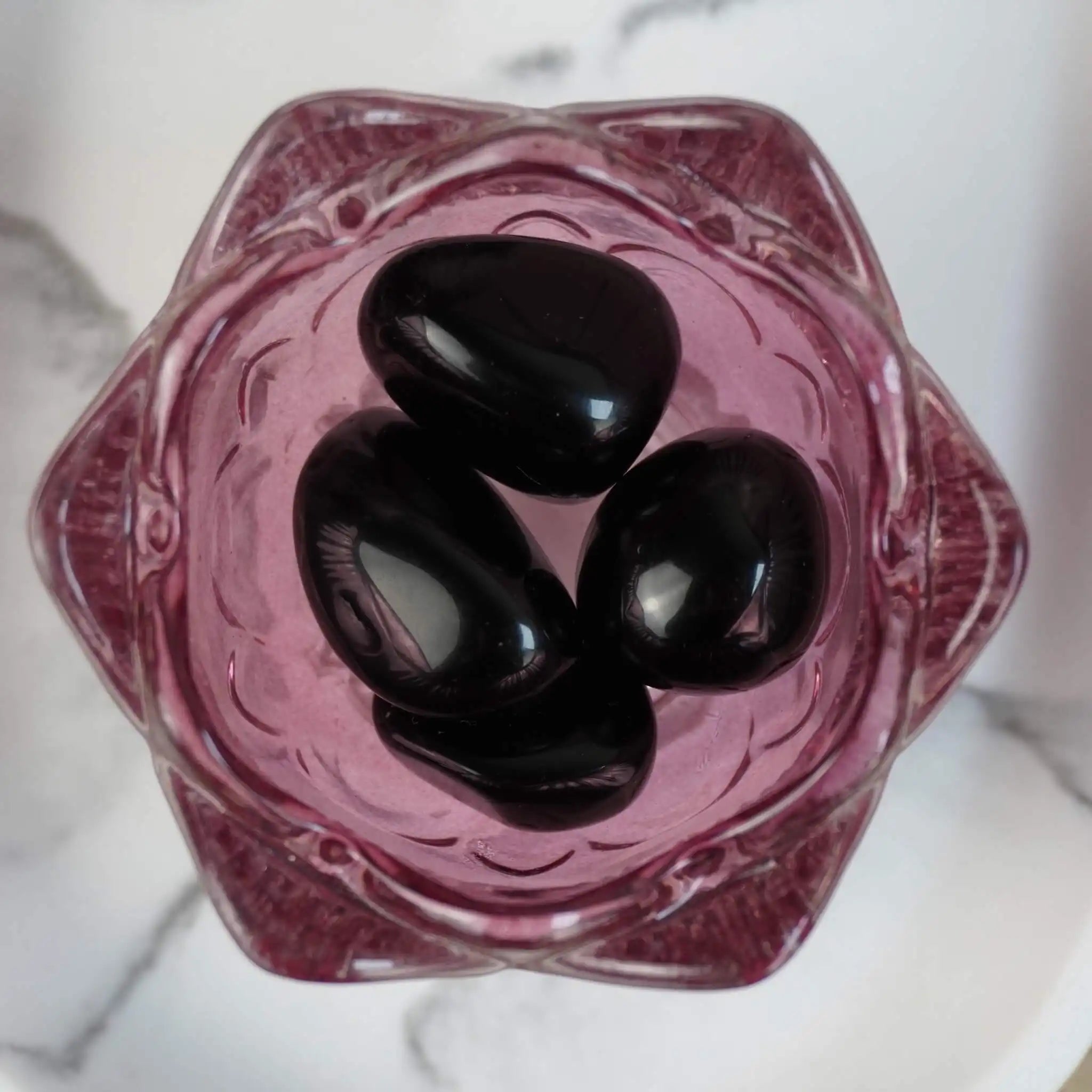 Vier schwarze Obsidian Trommelsteine in einer rosa Glasschale