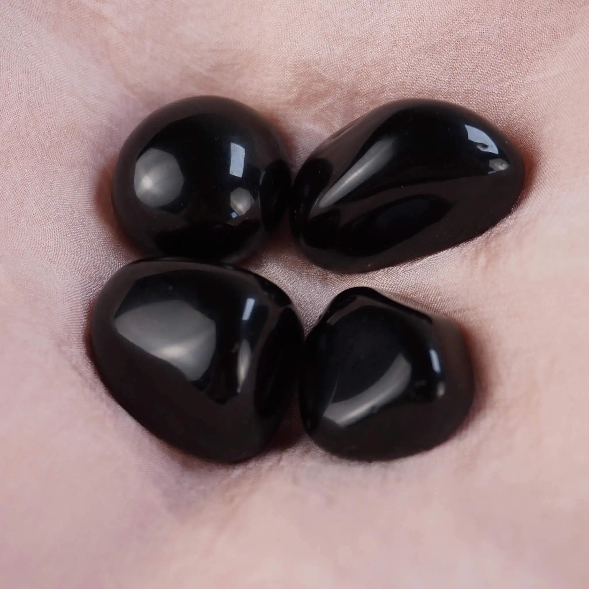 Vier Obsidian Trommelsteine auf rosa Satin-Stoff