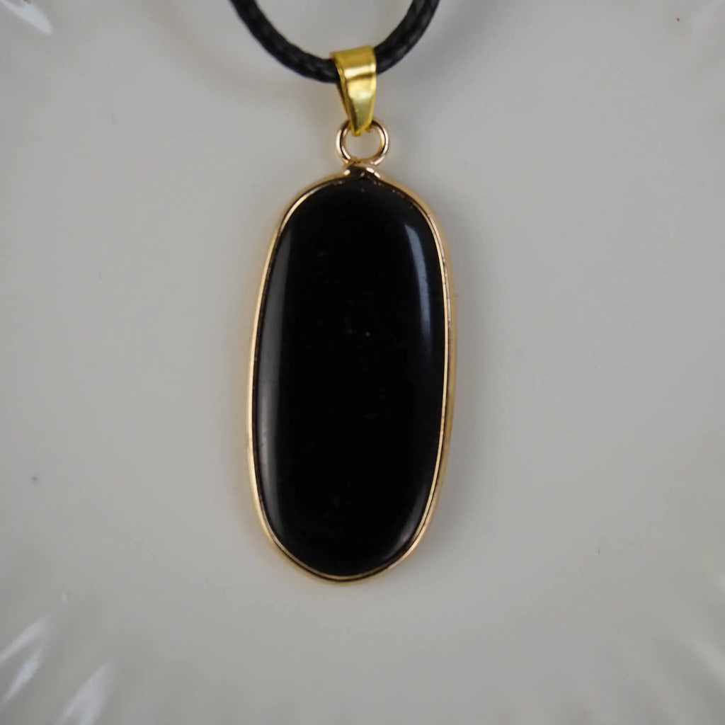 Schwarzer Onyx-Anhänger mit goldfarbener Umrandung an schwarzem Band, vor hellem Hintergrund
