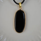 Schwarzer Onyx-Anhänger mit goldfarbener Umrandung an schwarzem Band, vor hellem Hintergrund