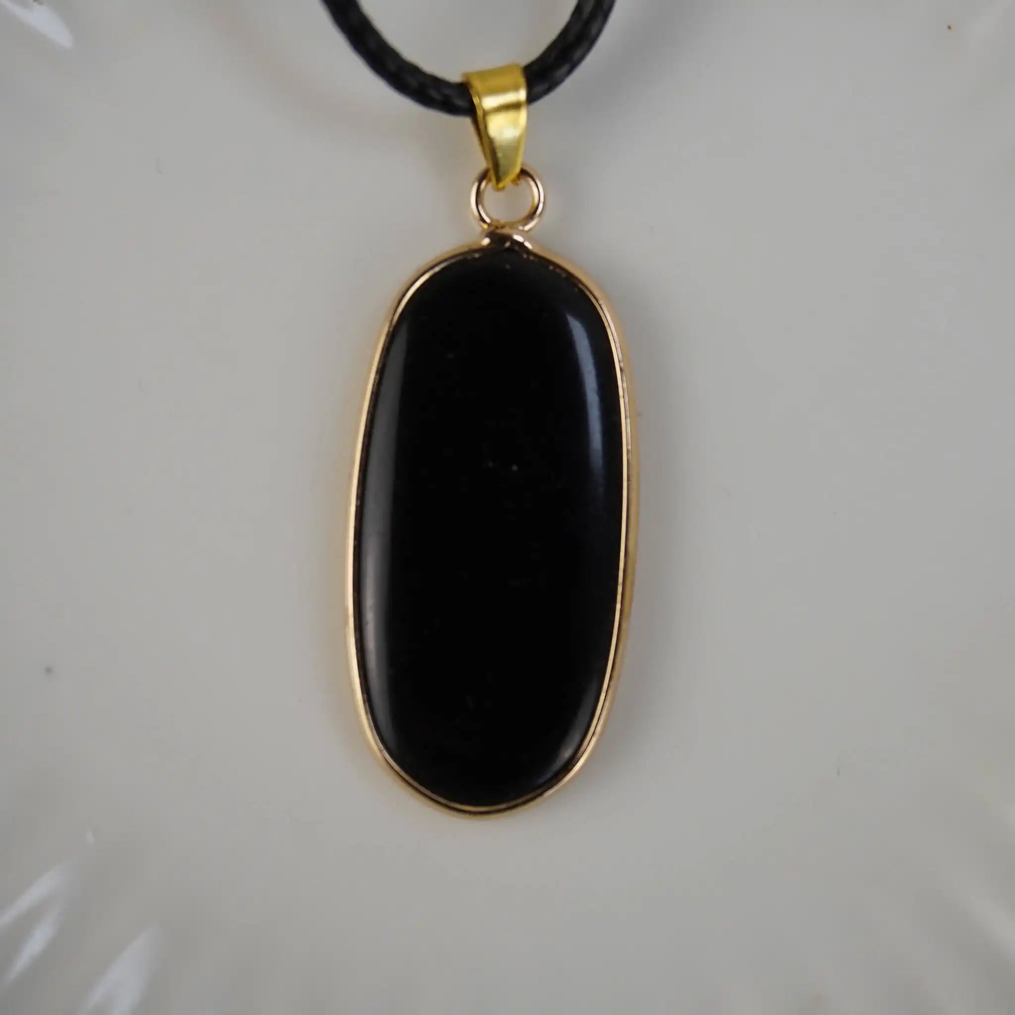 Schwarzer Onyx-Anhänger mit goldfarbener Umrandung an schwarzem Band, vor hellem Hintergrund