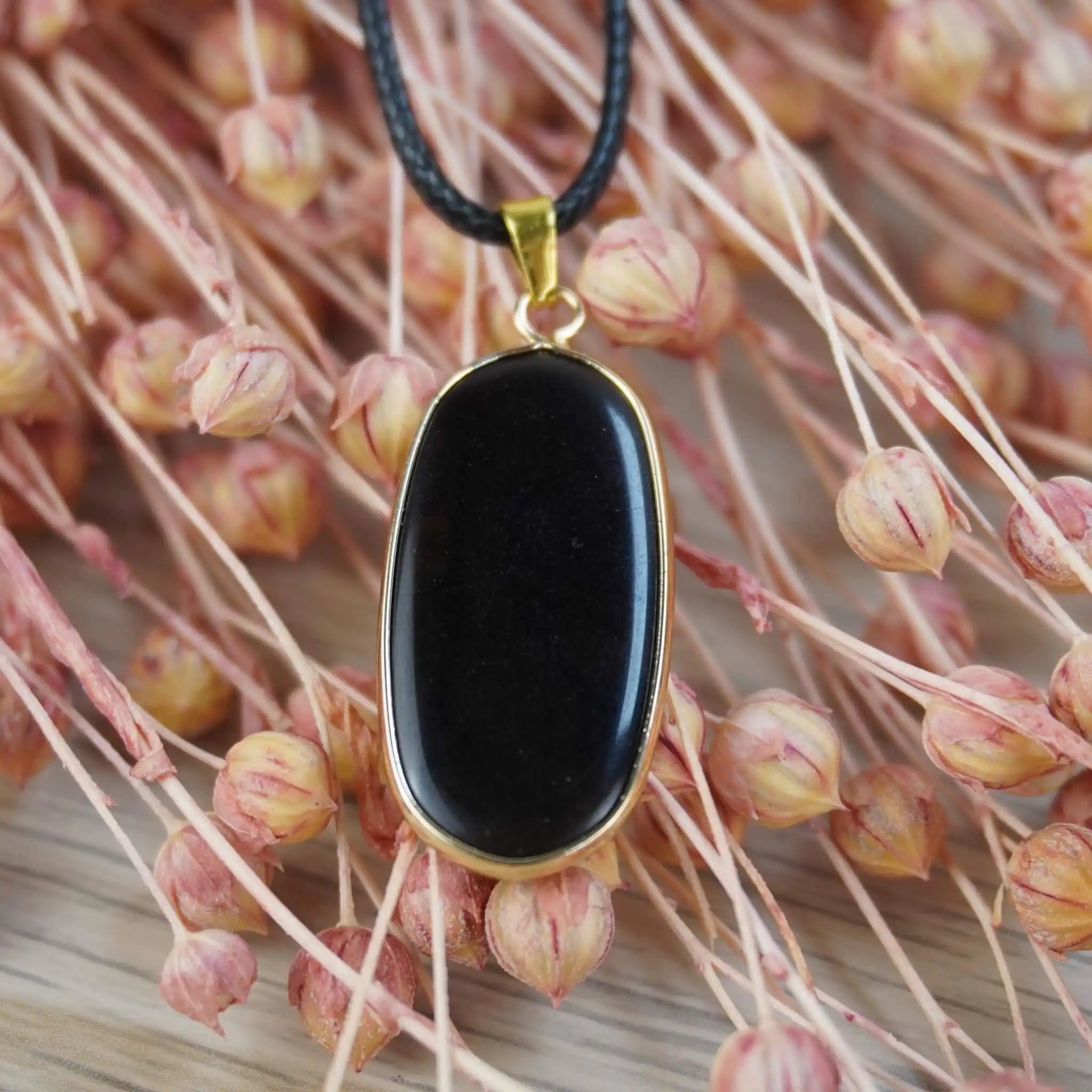 Schwarzer Onyx-Anhänger an schwarzem Band vor rosa Trockenblumen