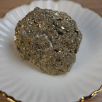 Pyrit Rohstein mit goldglänzender Oberfläche auf einem weißen Teller