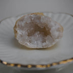Einzelne Quarz Geode mit kristalliner Mitte auf weißer Schale mit Goldrand