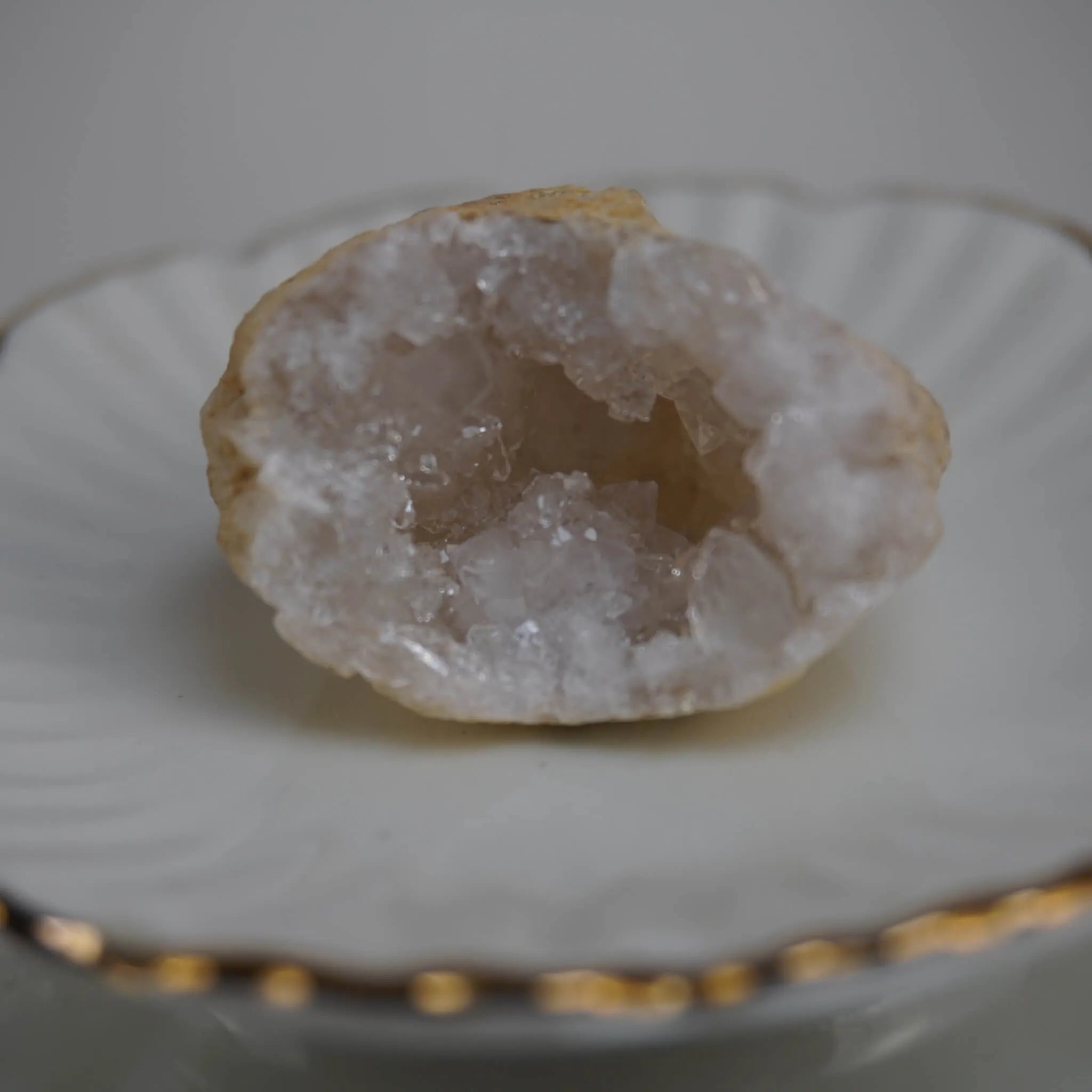 Einzelne Quarz Geode mit kristalliner Mitte auf weißer Schale mit Goldrand