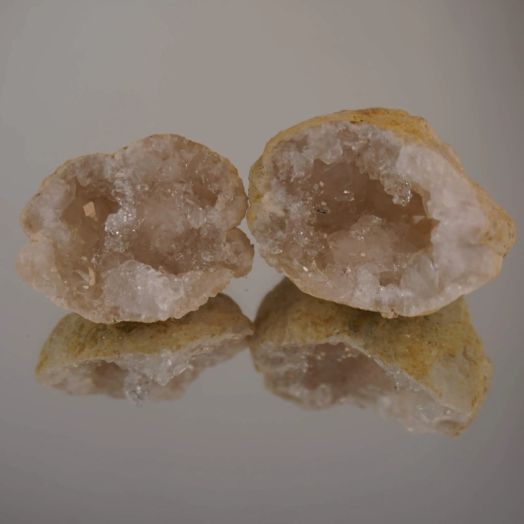 Zwei aufgebrochene Quarz Geoden mit Spiegelung auf glänzender Unterlage