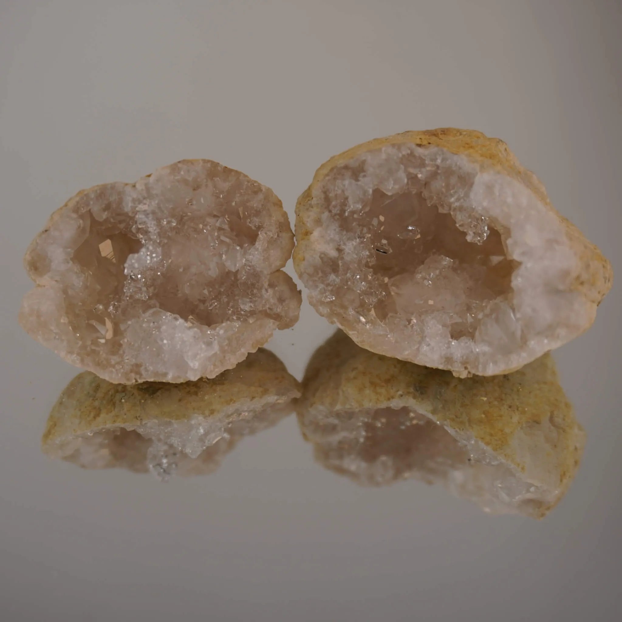 Zwei aufgebrochene Quarz Geoden mit Spiegelung auf glänzender Unterlage