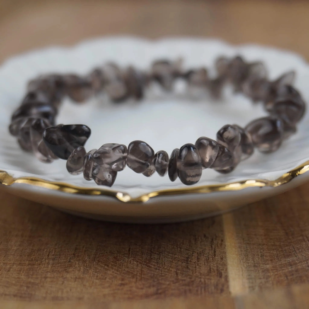 Rauchquarz‑Splitterarmband auf weißem Teller mit Goldrand