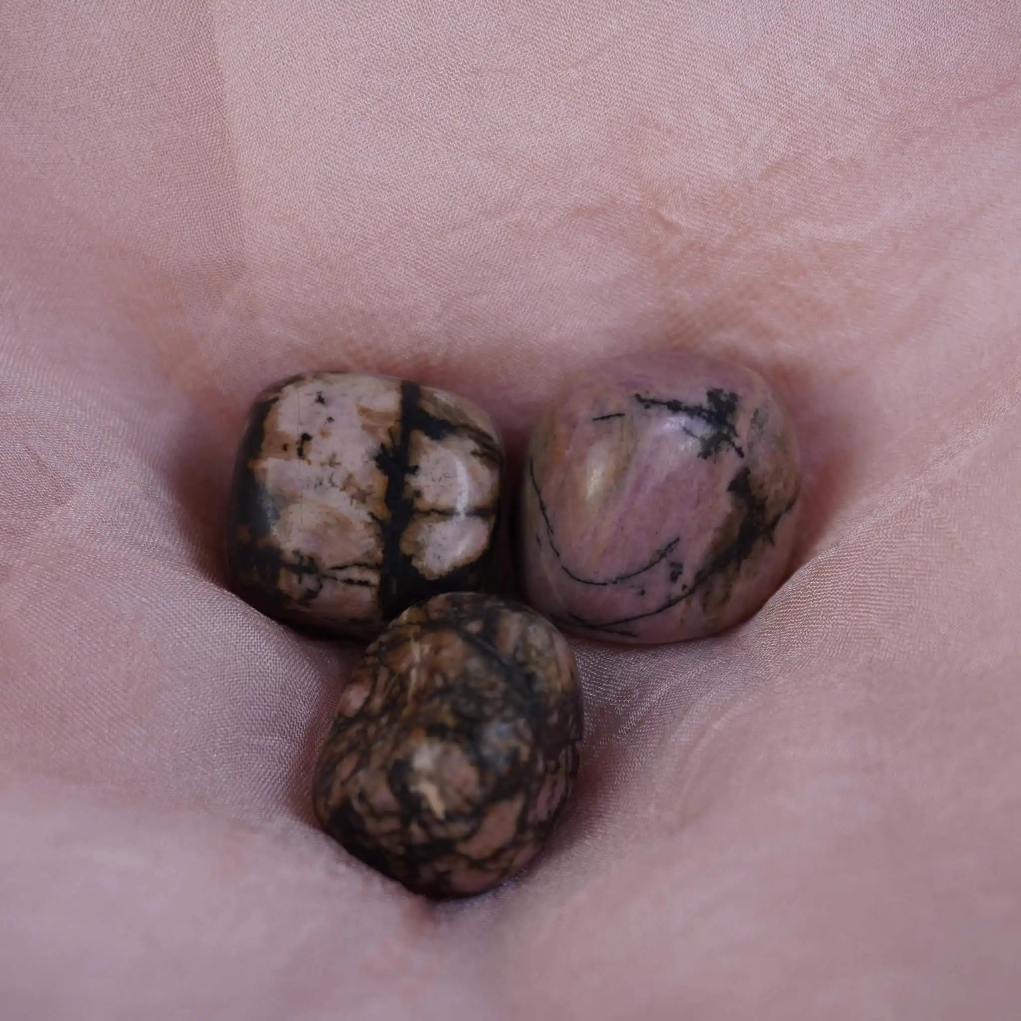 Rhodonit Trommelsteine in Rosa mit schwarzen Adern auf rosa Stoff