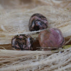 Rhodonit Trommelsteine auf hellem Naturmaterial mit warmen Farben