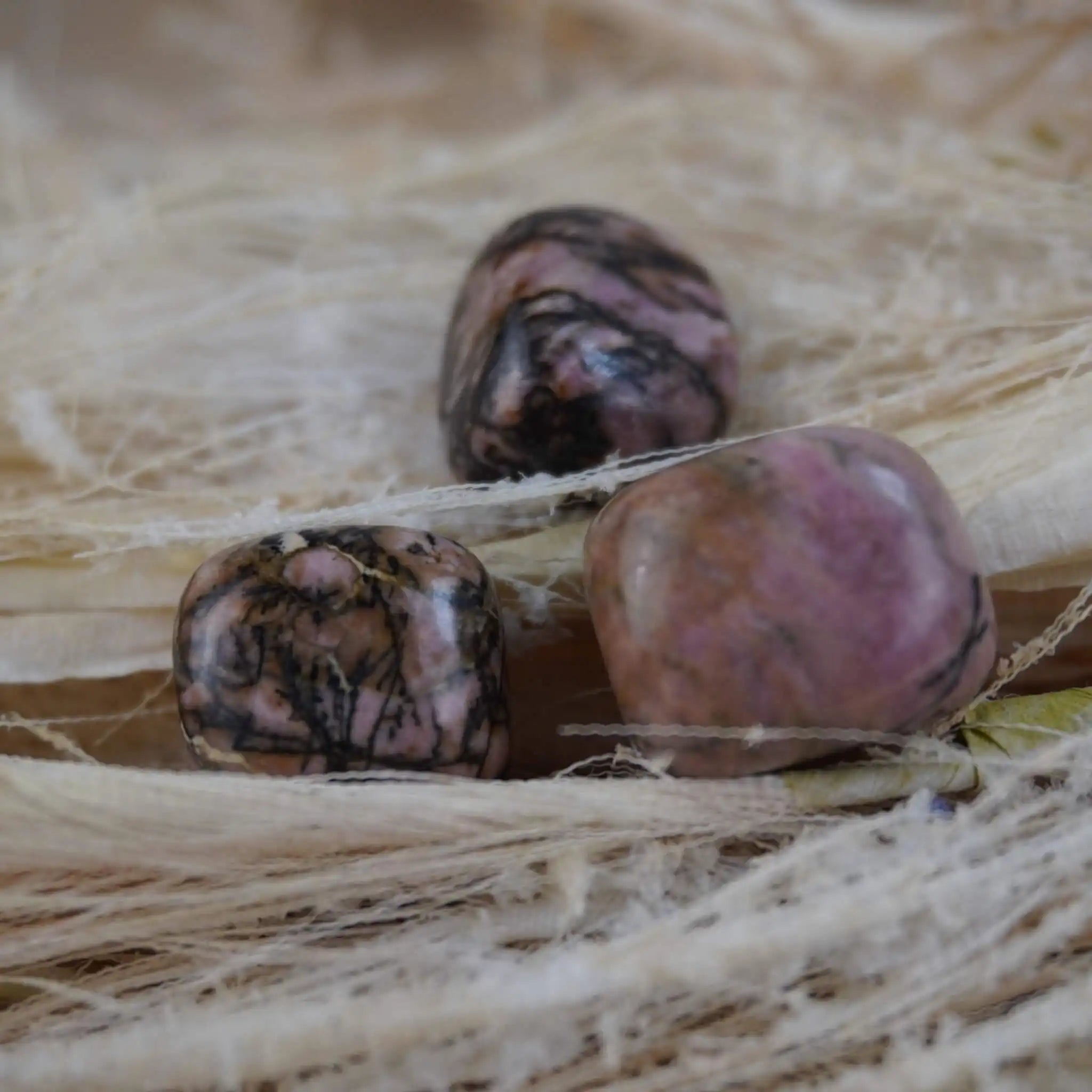 Rhodonit Trommelsteine auf hellem Naturmaterial mit warmen Farben
