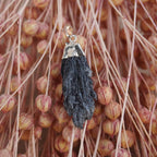 Roher schwarzer Kyanit Kettenanhänger mit silberner Metallfassung vor rosa Trockenblumen