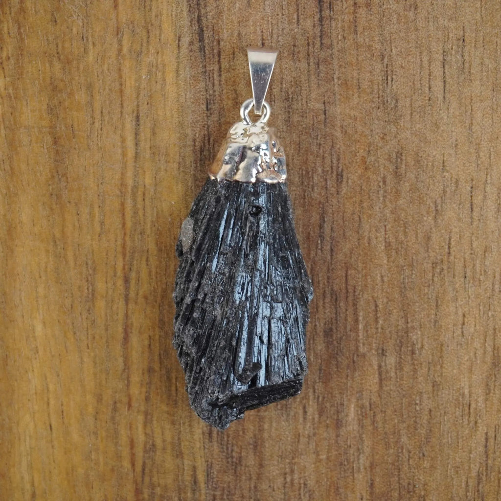 Roher schwarzer Kyanit Kettenanhänger mit polierter Metallkappe auf Holzuntergrund