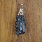 Roher schwarzer Kyanit Kettenanhänger mit polierter Metallkappe auf Holzuntergrund