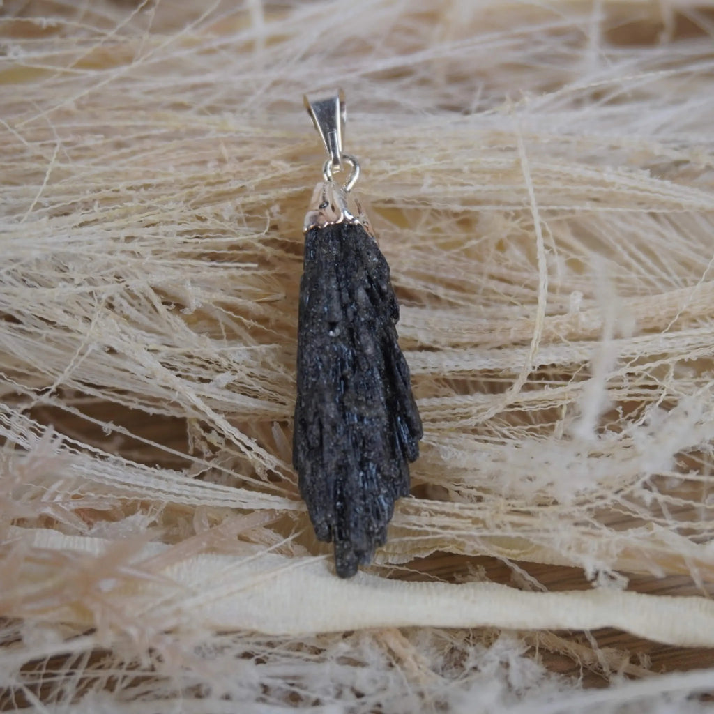 Roher schwarzer Kyanit Kettenanhänger mit silberfarbener Kappe auf hellen Naturfasern