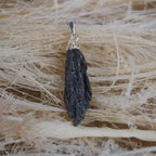 Roher schwarzer Kyanit Kettenanhänger mit silberfarbener Kappe auf hellen Naturfasern