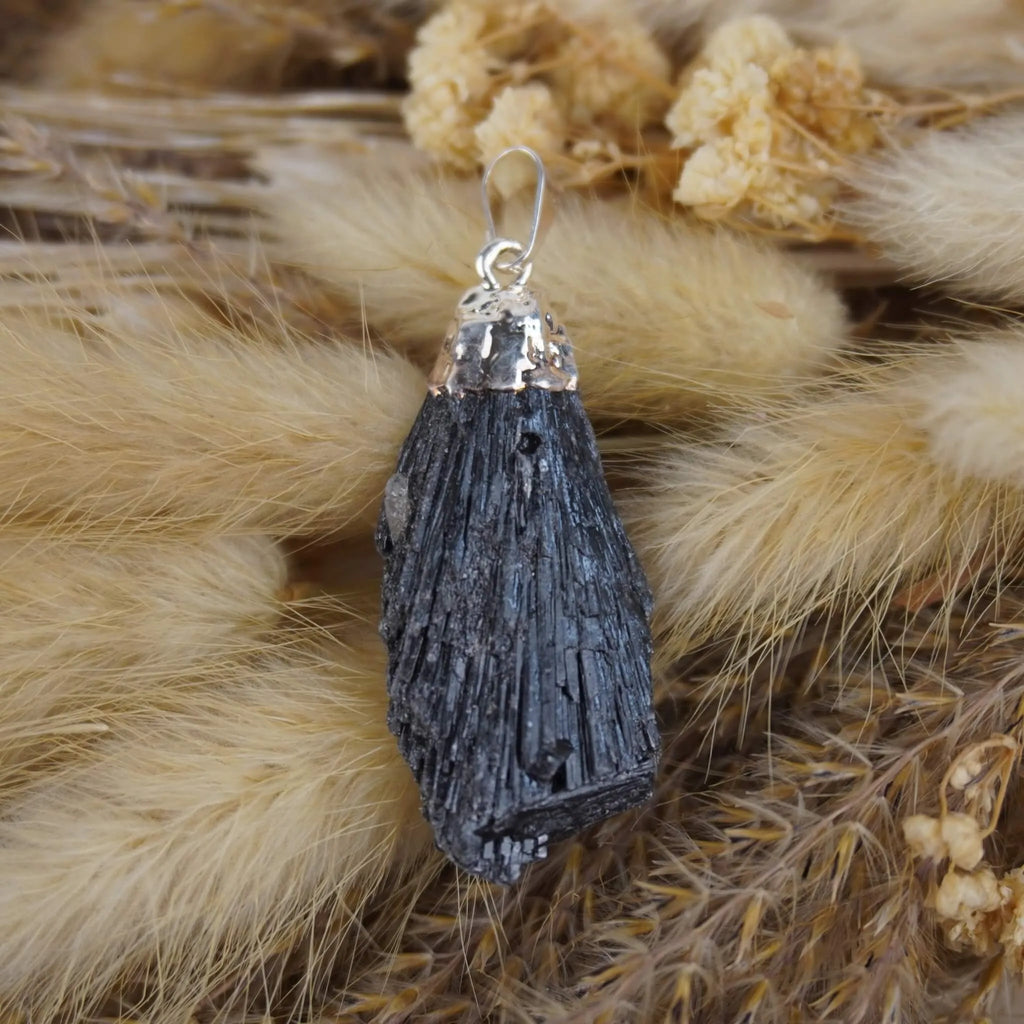 Roher schwarzer Kyanit Kettenanhänger mit Silberfassung auf beigen Trockenpflanzen