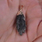 Roher schwarzer Kyanit Kettenanhänger mit silberfarbener Fassung in einer Hand liegend