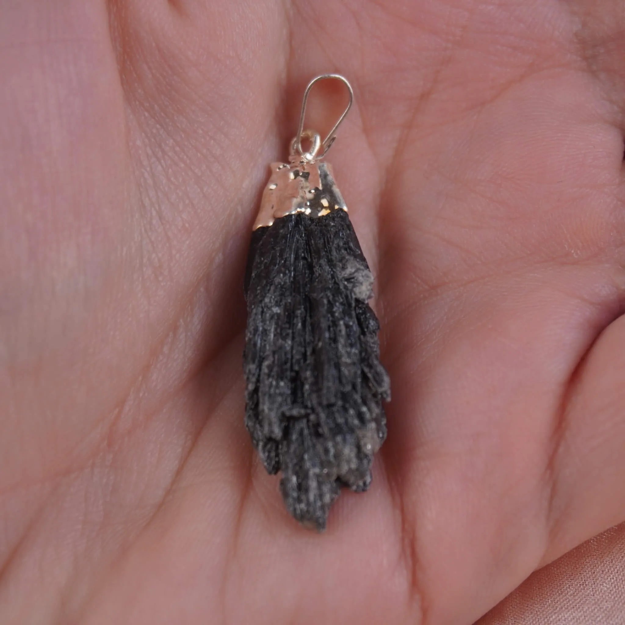 Roher schwarzer Kyanit Kettenanhänger mit silberfarbener Fassung in einer Hand liegend