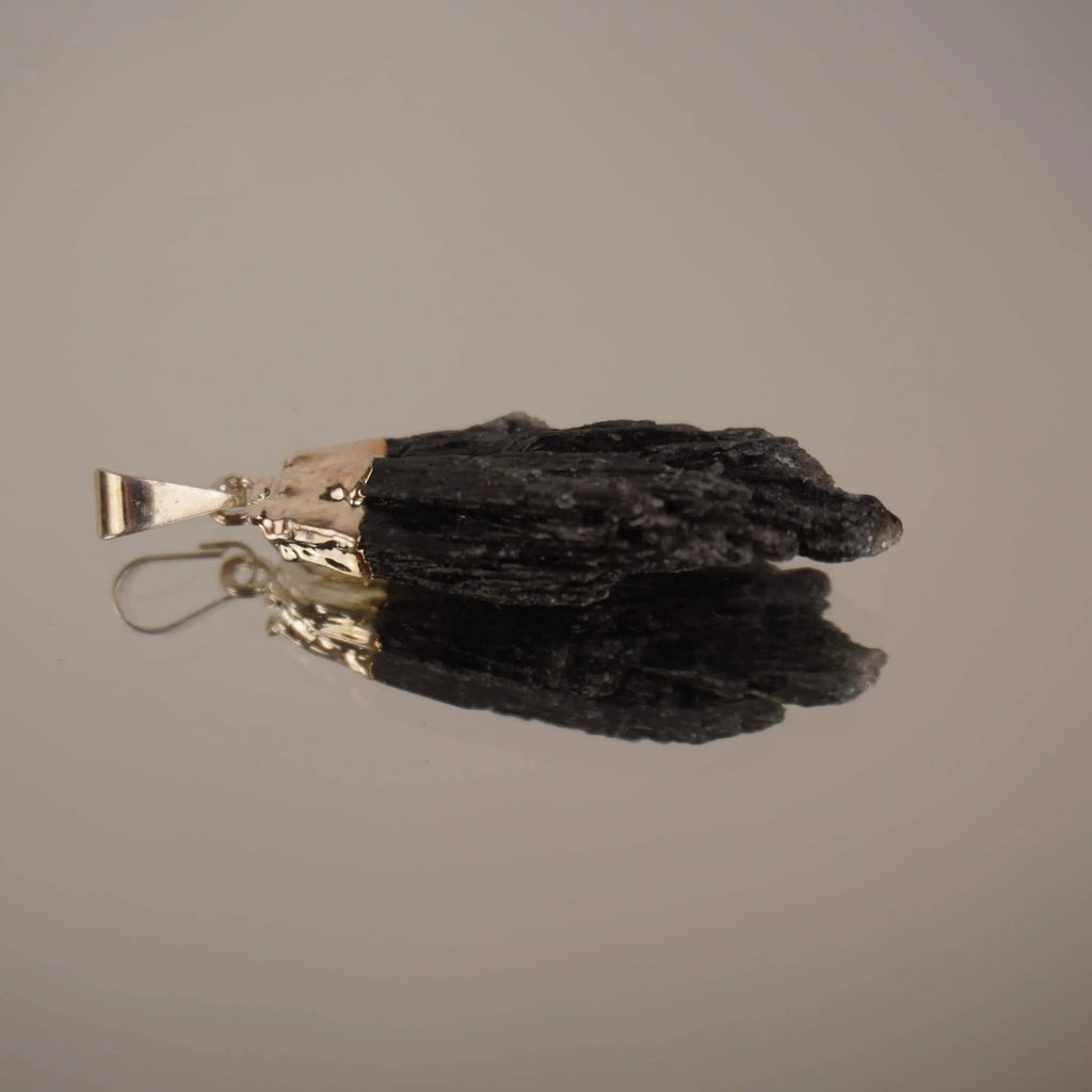 Liegender roher schwarzer Kyanit Kettenanhänger mit Spiegelung auf glänzender Fläche