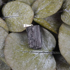 Roher schwarzer Turmalin Kettenanhänger dekoriert auf grünen Eukalyptusblättern