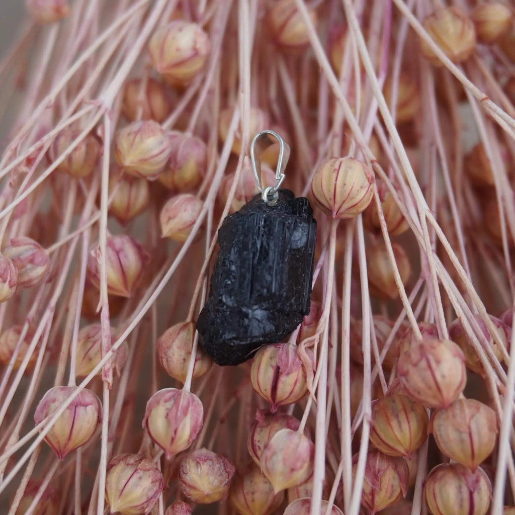 Roher schwarzer Turmalin Kettenanhänger dekoriert vor rosa Trockenblumen