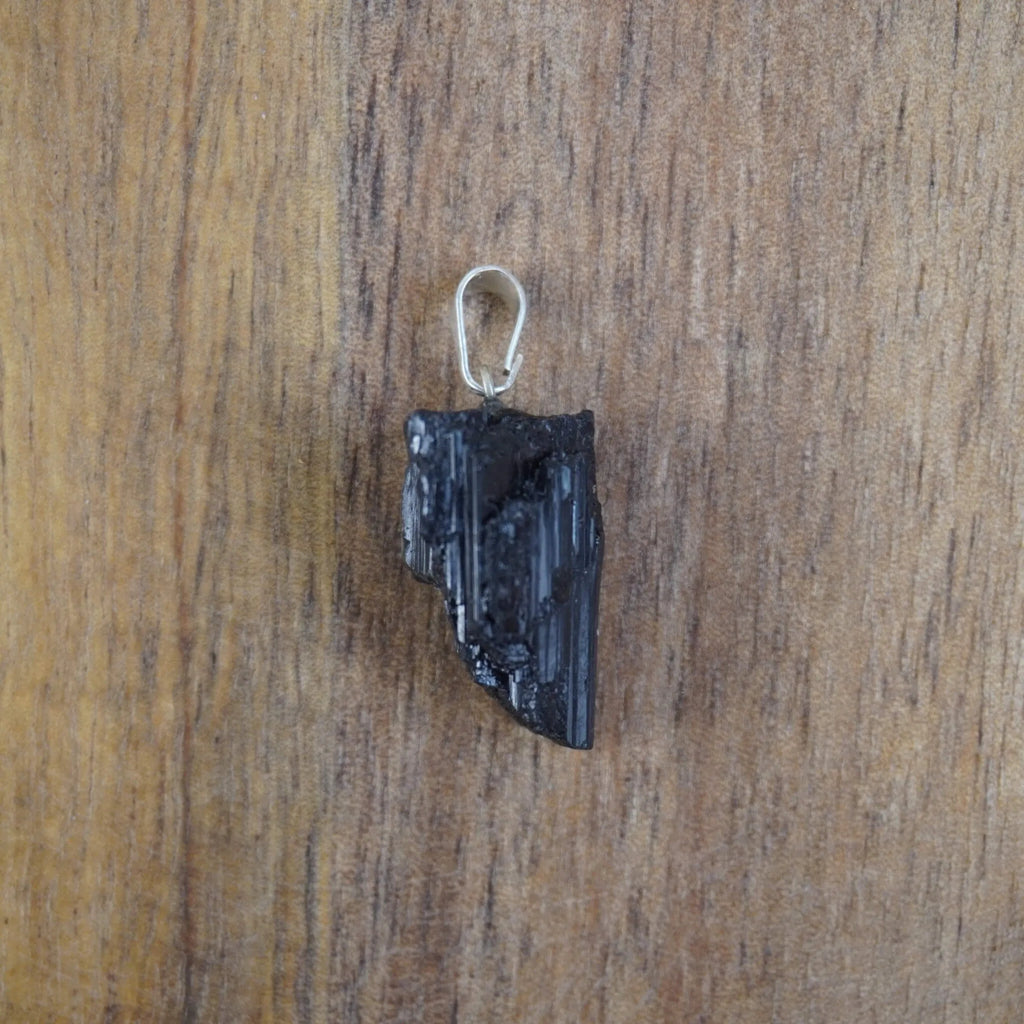 Roher schwarzer Turmalin Kettenanhänger mit silberner Öse vor Holzuntergrund