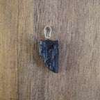 Roher schwarzer Turmalin Kettenanhänger mit silberner Öse vor Holzuntergrund