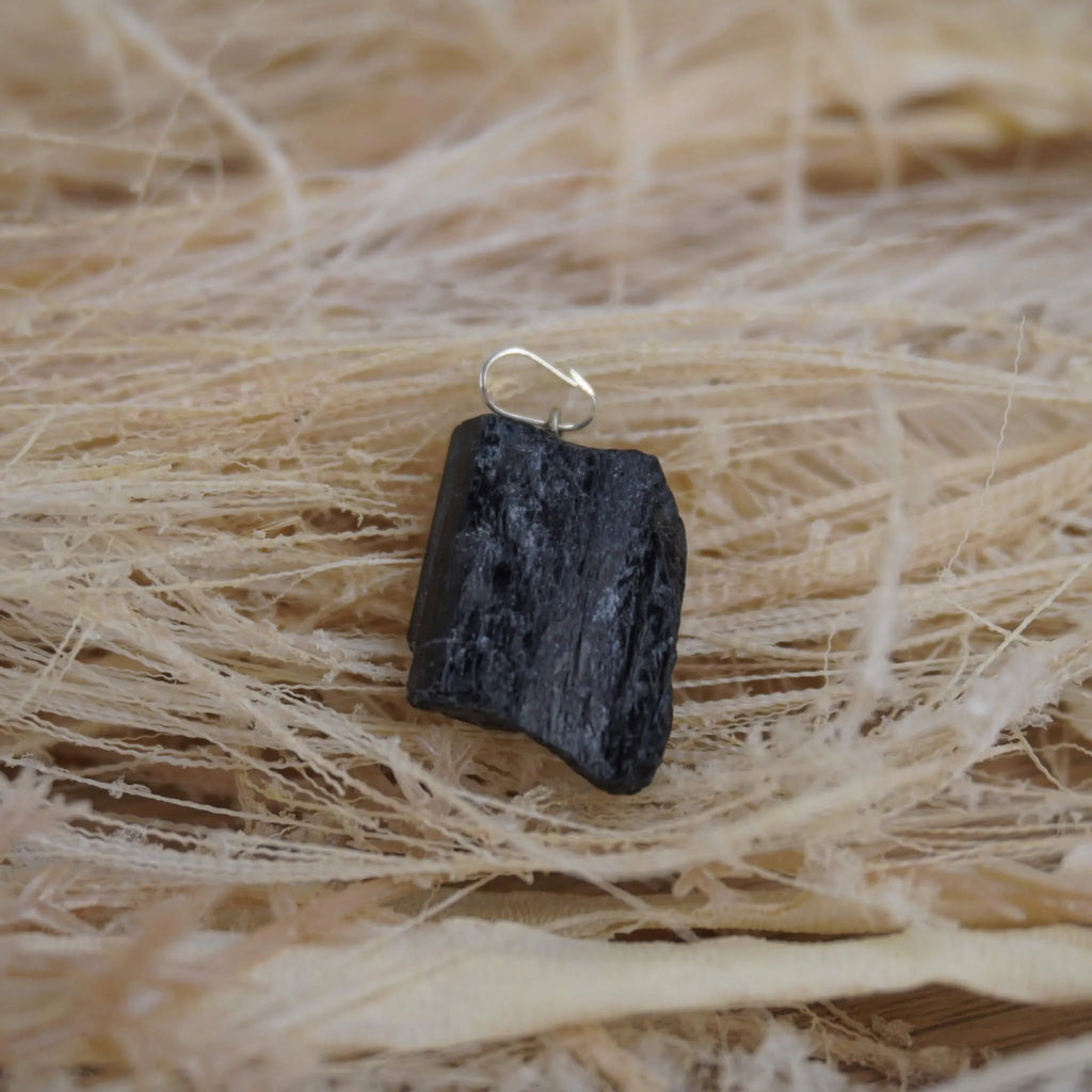 Roher schwarzer Turmalin Kettenanhänger mit Öse auf hellen Naturfasern arrangiert