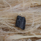 Roher schwarzer Turmalin Kettenanhänger mit Öse auf hellen Naturfasern arrangiert