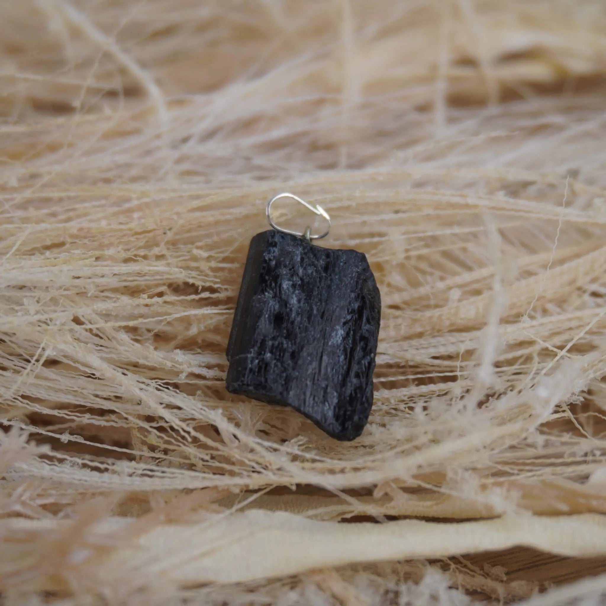 Roher schwarzer Turmalin Kettenanhänger mit Öse auf hellen Naturfasern arrangiert