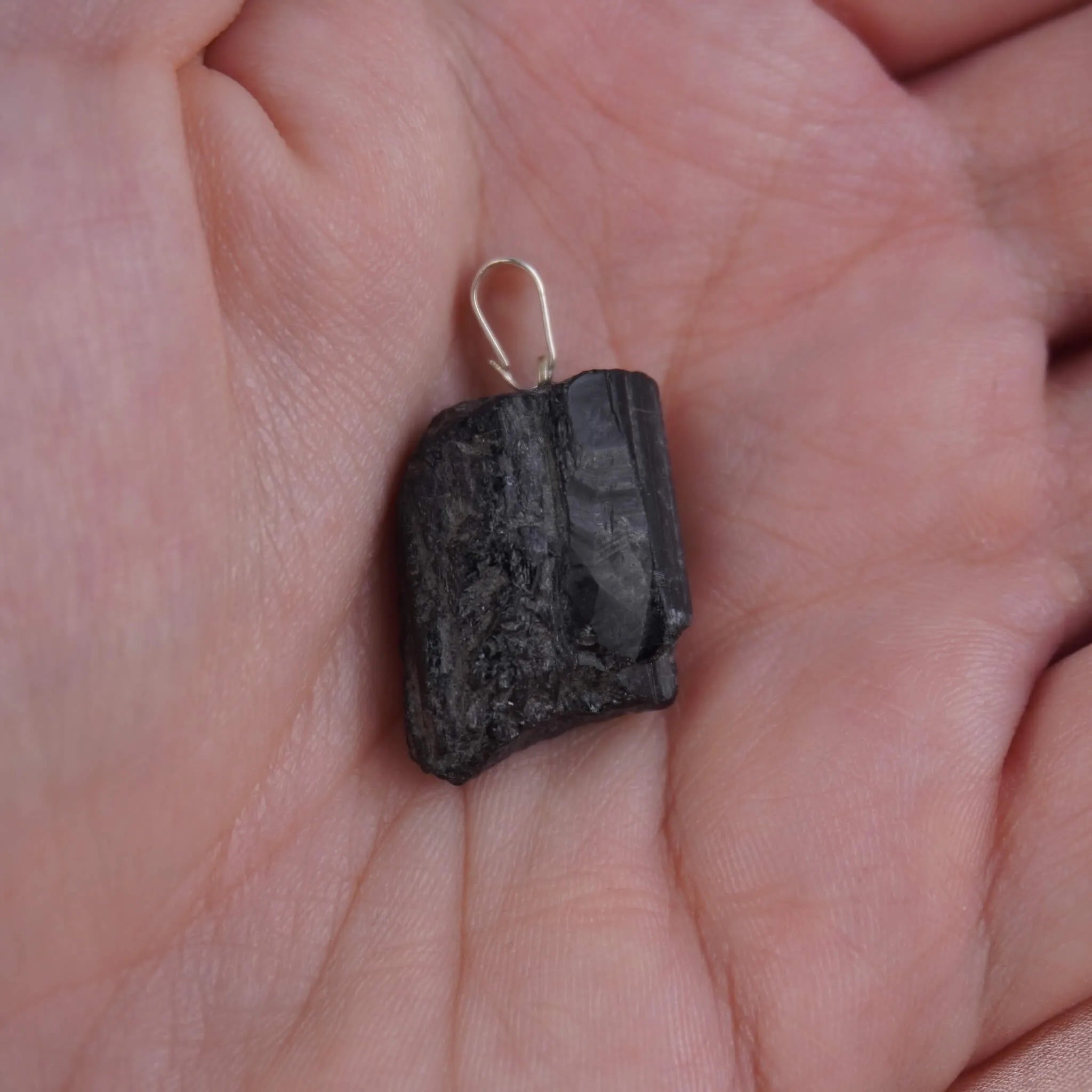 Roher schwarzer Turmalin Kettenanhänger mit silberfarbener Öse in einer Hand liegend