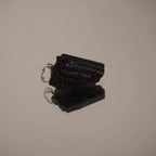 Liegender roher schwarzer Turmalin Kettenanhänger mit Spiegelung auf glänzender Fläche