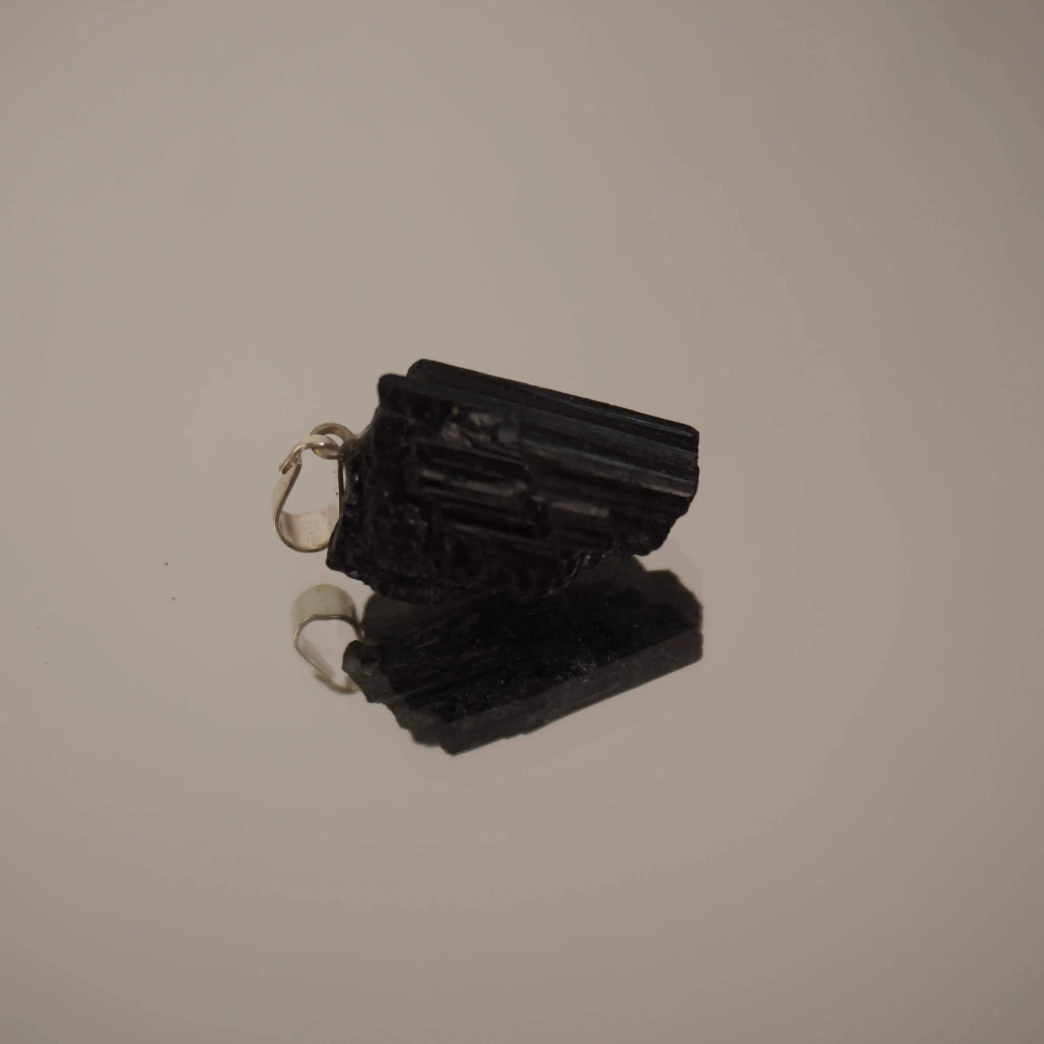 Liegender roher schwarzer Turmalin Kettenanhänger mit Spiegelung auf glänzender Fläche