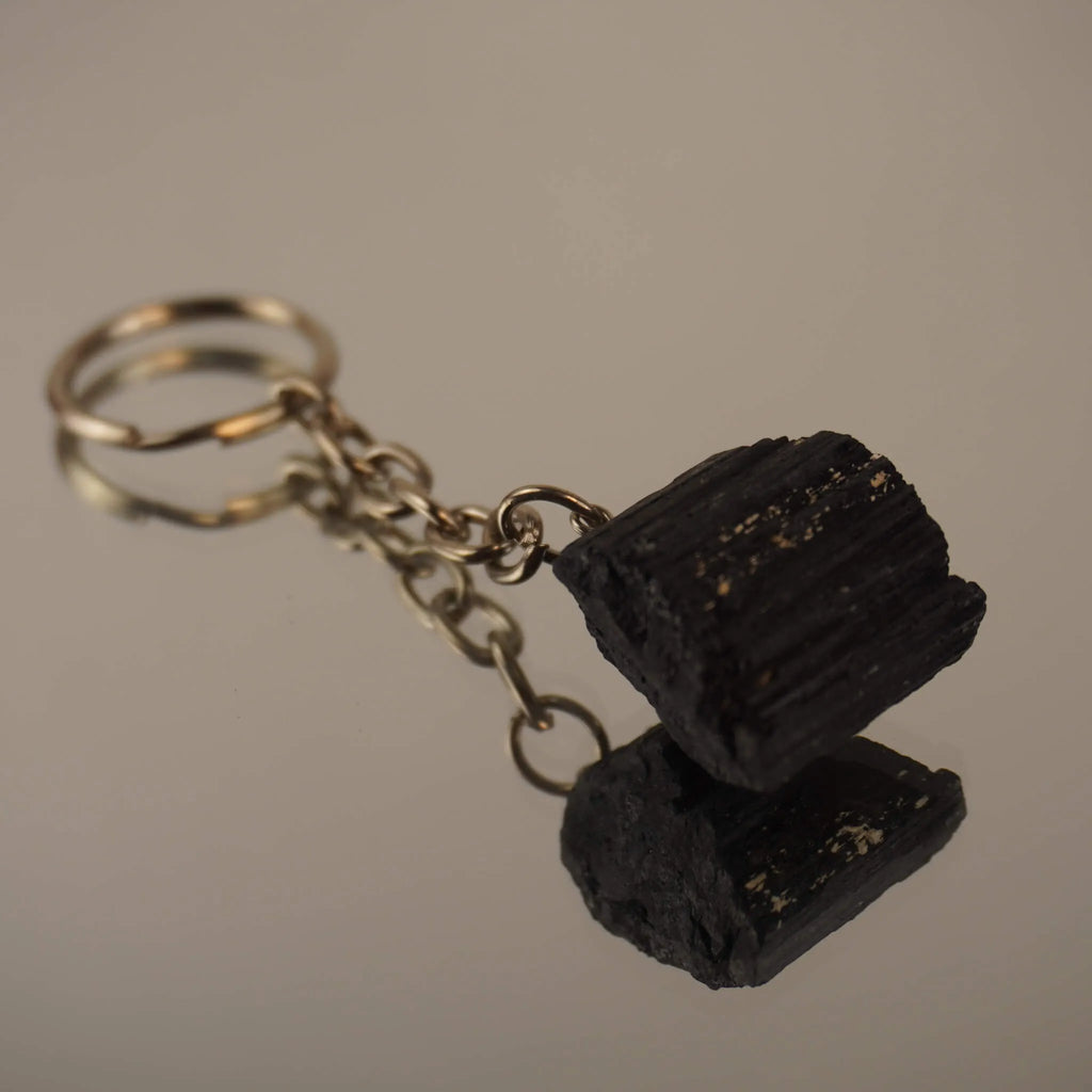 Roher schwarzer Turmalin Schlüsselanhänger auf spiegelnder Fläche mit Reflexion