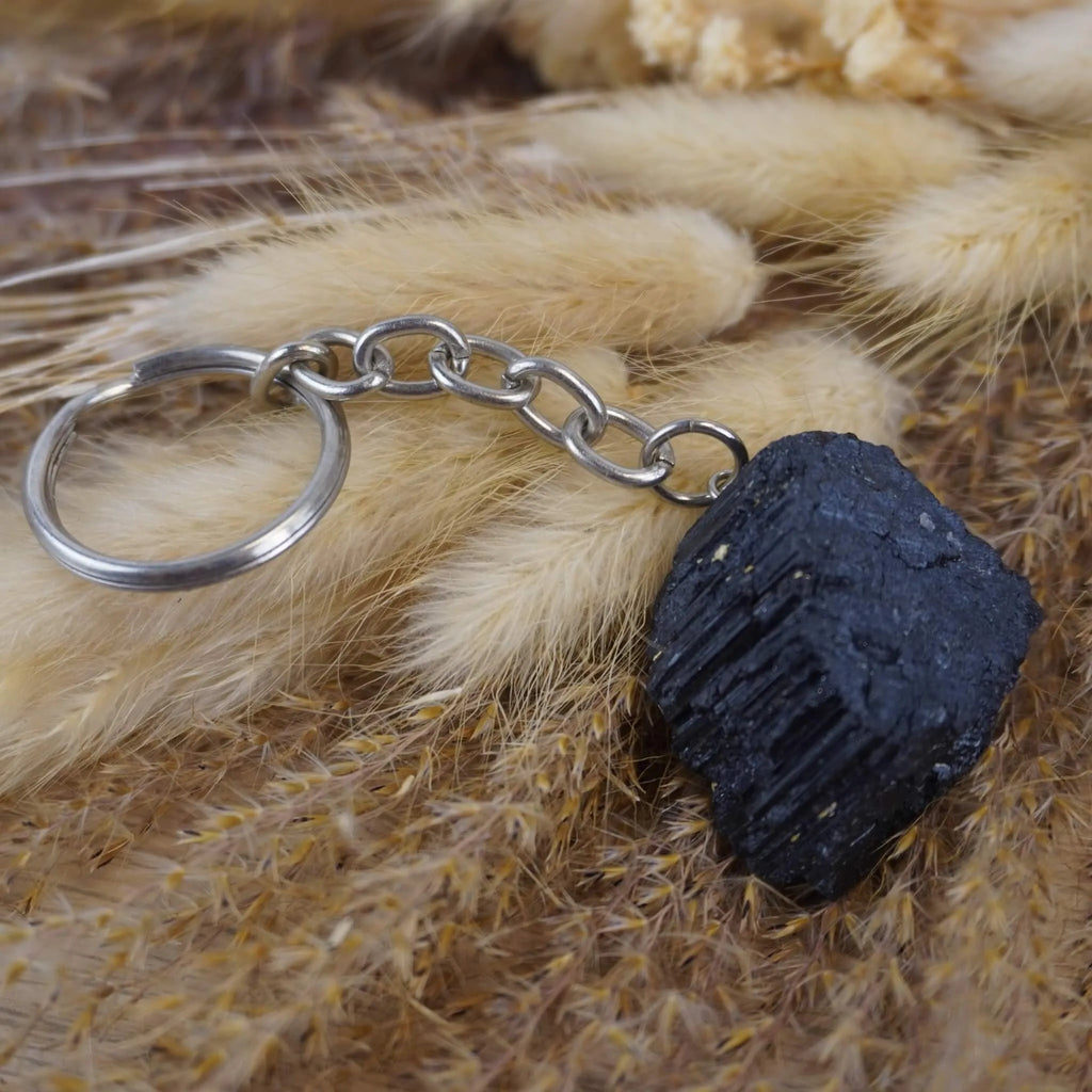 Roher schwarzer Turmalin Schlüsselanhänger auf beigen flauschigen Trockenpflanzen dekoriert