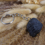Roher schwarzer Turmalin Schlüsselanhänger auf beigen flauschigen Trockenpflanzen dekoriert