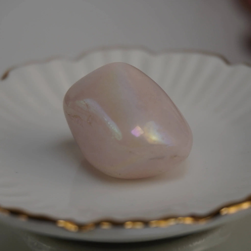 Einzelner rosa Angel Aura Trommelstein mit Perlmuttglanz auf weißer Schale mit Goldrand