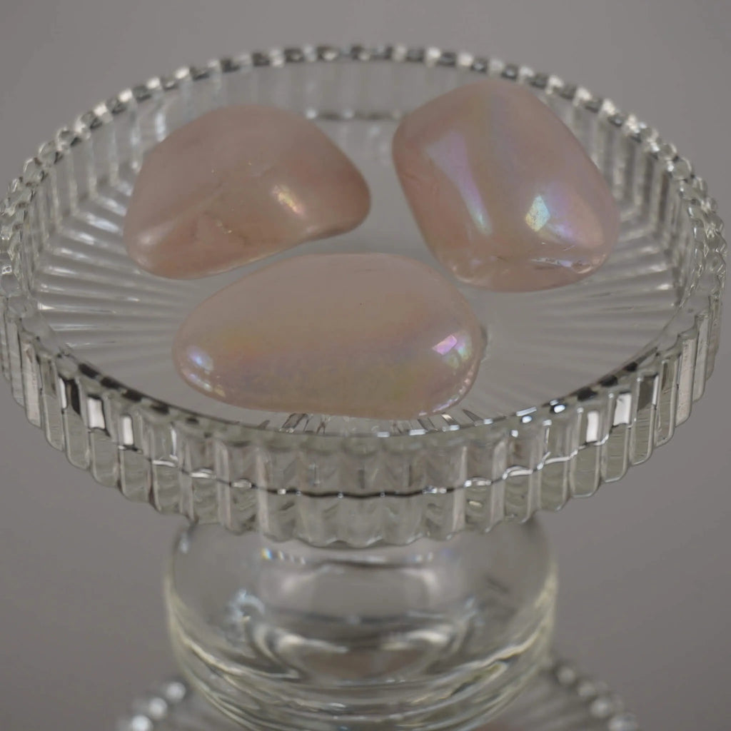 Drei rosa Angel Aura Trommelsteine mit irisierendem Glanz auf einem erhöhten Glasteller
