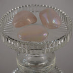 Drei rosa Angel Aura Trommelsteine mit irisierendem Glanz auf einem erhöhten Glasteller