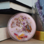 Zartrosa Duftteelicht mit Rosenquarz und Blüten, künstlerisch zwischen Büchern und Kristallen platziert