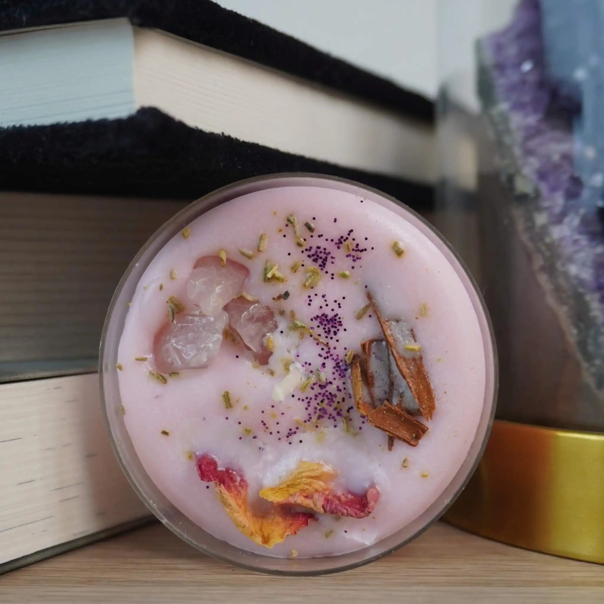 Zartrosa Duftteelicht mit Rosenquarz und Blüten, künstlerisch zwischen Büchern und Kristallen platziert