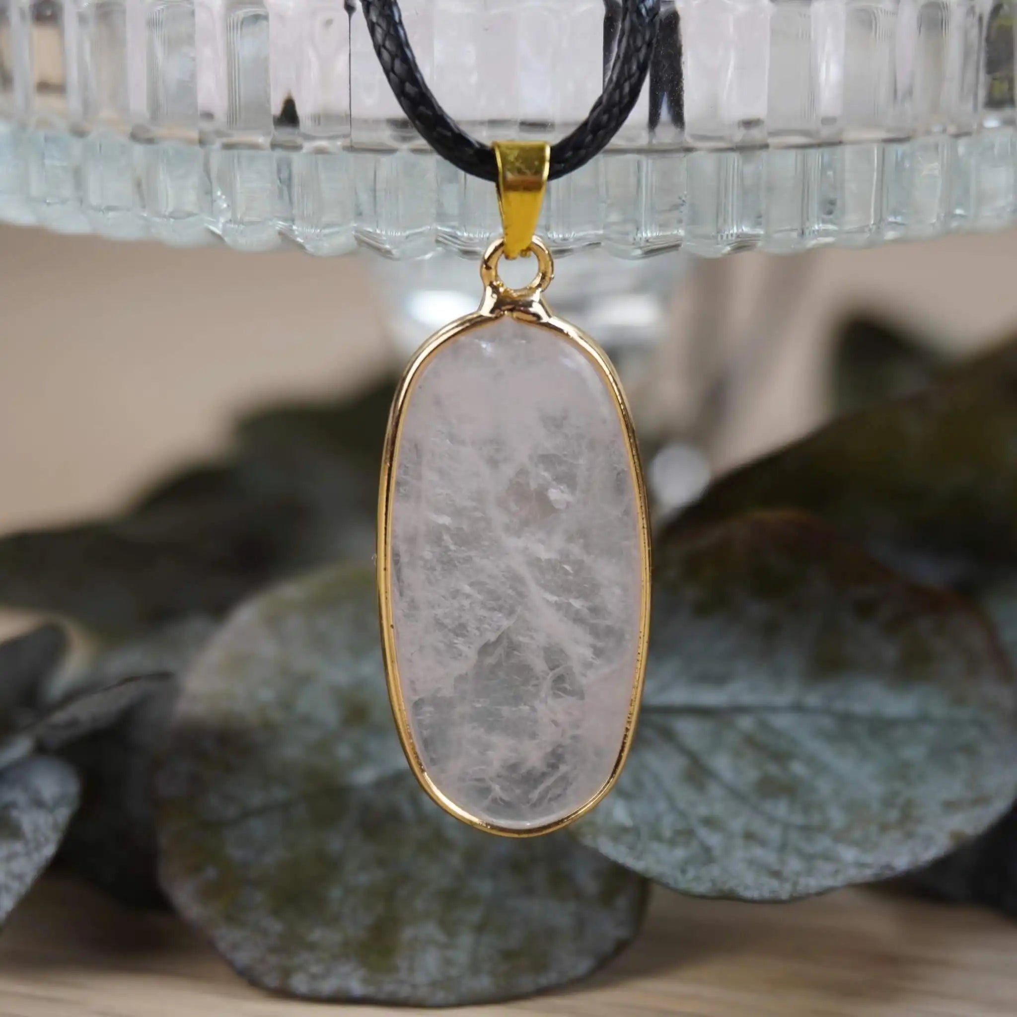 Edle Halskette mit Rosenquarz-Anhänger in goldfarbener Fassung vor Glas und Blättern